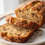 Moist banana bread slice with crackly sugar crust on rustic cutting board