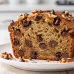 Moist chocolate chip banana bread slice on a rustic wooden cutting board.