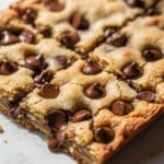 Freshly baked chocolate chip cookie bars with gooey chocolate chips on a rustic wooden table.