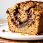 Moist cinnamon swirl banana bread slice on a rustic wooden cutting board.