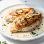 Creamy garlic parmesan chicken in skillet with sauce and fresh herbs.