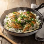 Creamy smothered chicken and rice in a rustic skillet with parsley garnish.