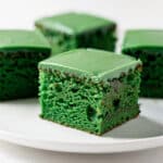 Moist green velvet cake square with cream cheese frosting on a white plate.
