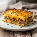 Cheesy sausage hash brown breakfast casserole slice on white plate.