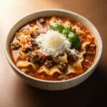 High protein lasagna soup in a rustic bowl with cheese and basil garnish