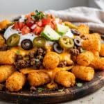 Loaded tater tot nachos with seasoned beef and melted cheese on a wooden board.