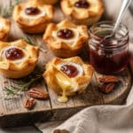 Mini Brie Bites with puff pastry and fig jam on a wooden board.