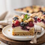 Mixed berry cheesecake crumb bars with creamy swirl and golden topping.