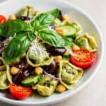 Creamy pesto tortellini salad with fresh vegetables and olives in close up