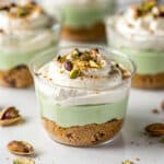 Layered pistachio pudding dessert cups with creamy vanilla topping and pistachios.