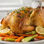 Golden brown lemon herb roast chicken on a rustic wooden cutting board.