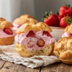 Golden strawberry cream puffs with fresh fruit filling on rustic table.