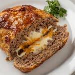 Stuffed meatloaf recipe reveals molten cheese pull in overhead food photography.