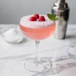 Vibrant pink Valentine's mocktail in a coupe glass with raspberry garnish.