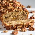 Moist walnut banana bread slice with toasted nuts on rustic cutting board