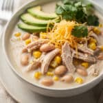 Creamy white chicken chili with corn in a rustic bowl garnished with avocado and cilantro.