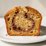 Moist cinnamon swirl banana bread slice with walnuts on a wooden board.