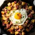 Crispy corned beef hash with potatoes and a fried egg in skillet