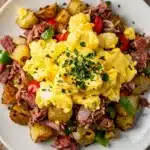 Hearty corned beef hash breakfast scramble in a rustic cast iron skillet.