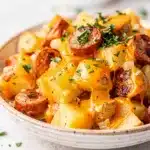 Creamy crockpot cheesy potatoes with smoked sausage in rustic ceramic bowl.