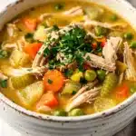 Creamy chicken pot pie soup in a rustic bowl with a flaky biscuit garnish.