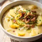 Creamy potato leek soup in a white bowl garnished with bacon and chives
