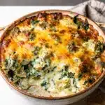 Creamy baked spinach artichoke dip in a rustic white ceramic dish.