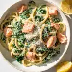 Creamy spinach salmon pasta with fettuccine and parmesan cheese on white plate.