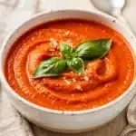Creamy tomato basil soup in a rustic bowl with fresh basil garnish.