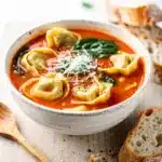 Creamy tomato tortellini soup with spinach and parmesan in a white bowl