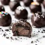 Oreo balls with glossy chocolate coating and creamy filling on white plate.