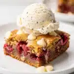 Raspberry white chocolate blondies with vanilla ice cream on rustic table.