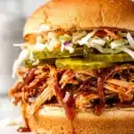 Slow cooker BBQ pulled chicken sandwiches with glossy sauce on rustic wooden board