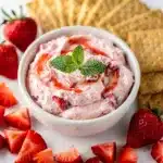Creamy strawberry cheesecake dip in a bowl with fresh fruit and cookie dippers.