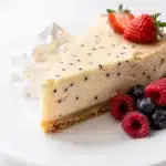 Creamy vanilla bean cheesecake slice with raspberries and a graham cracker crust.