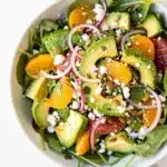 Close up of creamy avocado and glossy citrus segments in vibrant salad