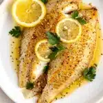 Crispy lemon pepper tilapia with buttery sauce and fresh lemon slices.