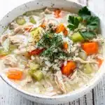 Creamy chicken and rice soup in a rustic bowl with dill garnish.