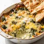 Creamy spinach artichoke dip with golden cheese topping and tortilla chips.
