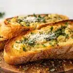 Golden brown garlic bread slices on a rustic wooden cutting board with parsley garnish