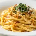 Garlic butter pasta with parsley and parmesan on a rustic white plate.