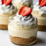 No bake cheesecake cups with strawberry topping in clear glass jars.