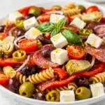 Colorful antipasto pasta salad with olives, peppers, and mozzarella pearls on wood.