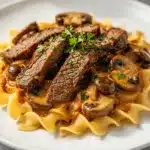 Creamy beef stroganoff with mushrooms and egg noodles on rustic table.