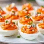 Buffalo deviled eggs with creamy filling and celery garnish on rustic board