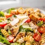 Creamy chicken Caesar pasta salad with rotini, romaine, and croutons in bowl.