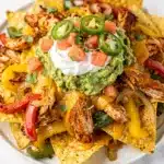 Crispy chicken fajita nachos loaded with colorful peppers, melted cheese, and fresh toppings.