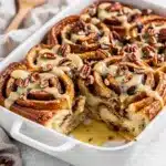 Golden brown cinnamon roll French toast bake with icing and pecans on a rustic table.