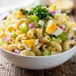 Creamy cold macaroni salad with celery, egg, and parsley in a bowl.