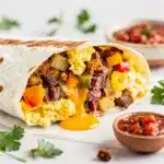Corned beef hash breakfast burrito with eggs cheese and salsa close up